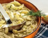 Schmorgurken in cremiger Soße mit Dill, daneben eine Zwiebel. So sehen sie aus, lecker und appetitlich.