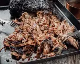 Saftiges Pulled Pork, frisch aus dem Smoker, wird mit Gabeln zerzupft und mit BBQ-Sauce beträufelt.