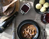 Herzhaftes Wild im Dutch Oven, serviert mit Klößen, Preiselbeeren und einem Glas Rotwein. Ein Festmahl!