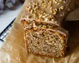 Omas Nusskuchen in Kastenform, mit Zuckerguss und gehackten Nüssen bestreut, wird auf Backpapier präsentiert.