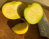 Zwei Hälften und ein Stück gelbe Zucchini liegen auf einem Holzbrett neben einem Messer.