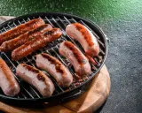 Mehrere Bratwürste brutzeln in der Pfanne auf einem Grill.