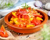 Buntes Peperonata-Gericht im Tontopf, garniert mit Kräutern. Ein Löffel zeigt ein Stück Paprika mit Zwiebeln, perfekt für das original Rezept.