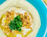 Cremiger Hummus, garniert mit Kichererbsen, Petersilie und Olivenöl. Ein authentisches Hummus Rezept original arabisch, serviert in einer blauen Schüssel.