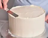 Eine Hand glättet mit einem Spachtel die cremige Buttercreme einer Torte, die für einen Geburtstag bestimmt ist.