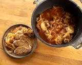 Herzhaftes Zwiebelfleisch im Dutch Oven, daneben eine Portion mit Brot auf einem Teller.