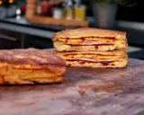 Zwei goldbraune Monte Cristo Sandwiches, gestapelt und mit Käse und Marmelade gefüllt, liegen auf einem Holzbrett.