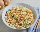 Schüssel mit gebratenem Eierreis wie beim Chinesen, garniert mit Erbsen und Karotten. Daneben liegen Stäbchen.