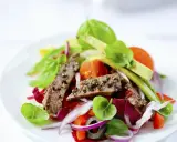 Frischer Salat mit zarten Rinderstreifen, Tomaten, roten Zwiebeln und Basilikum auf einem weißen Teller.
