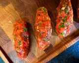 Rohe Cevapcici, bereit für das Rezept, liegen auf einem Holzbrett. Die Hackfleischröllchen sind mit Kräutern und Gewürzen verfeinert.