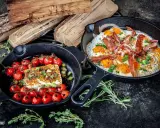 Zwei Gusseisenpfannen mit Eiern, Speck und Kirschtomaten mit Feta. Perfekt für low carb grillen.