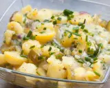Kartoffelsalat ohne Mayo, mit Gurken, Zwiebeln und Schnittlauch in einer Glasschüssel.