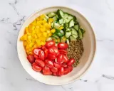 Zutaten für ein Linsensalat Rezept: gekochte Linsen, gewürfelte gelbe Paprika, Kirschtomaten und Gurkenstücke in einer Schüssel.