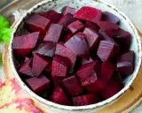 Schüssel mit gewürfelter roter Bete, bereit für die Kochzeit. Frische grüne Blätter und ein Herbstblatt liegen daneben.