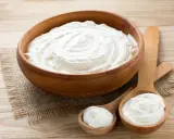 Cremiger Schmand in Holzschale und Löffeln. Ist Schmand gesund? Ja, in Maßen genossen, liefert er Kalzium und Proteine.
