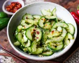 Erfrischender asiatischer Gurkensalat mit Sesam und Chili-Flocken, serviert in einer Schale mit Essstäbchen.