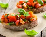 Zwei Bruschetta mit Tomaten und Basilikum, ein authentisches italienisches Rezept, auf rustikalem Holz.