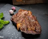 Perfekt gegrilltes Rib Eye Steak mit grobem Salz, Basilikum und Knoblauch auf schwarzem Stein.