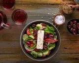 Frischer griechischer Salat mit Feta, Oliven, Tomaten, Gurken und Paprika, serviert mit Rotwein und Gewürzen.