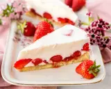 Ein Stück cremiger Erdbeerkuchen, der an Omas beste Kuchen Rezepte erinnert, mit frischen Erdbeeren und Blumen dekoriert.