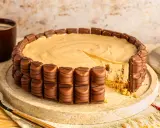 Eine köstliche Kinder Bueno Torte, umrandet von Schokoriegeln, mit einem Stück herausgeschnitten. Daneben eine Tasse Kaffee.