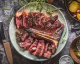 Saftiges, perfekt gegrilltes Bistecca alla Fiorentina, aufgeschnitten und mit Rosmarin garniert, daneben knusprige Kartoffeln.