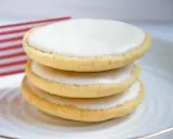 Drei amerikaner Kekse mit weißer Glasur auf einem Teller, im Hintergrund eine kleine US-Flagge. Ein leckeres amerikaner Rezept.