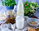 Ein Glas cremiges **ranch dressing** steht neben einem Glas mit brauner Soße, einem Salat und Brot.