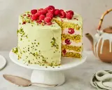 Himbeer Pistazien Torte mit frischen Beeren und knackigen Pistazien. Ein Stück ist angeschnitten und zeigt die saftige Füllung.