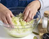 Hände mischen fein geschnittenen Weißkohl mit Kümmel in einer Glasschüssel. Ein Schritt im Sauerkraut Rezept.