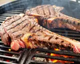 Zwei saftige tomahawk steaks brutzeln auf dem Grill. Rauch steigt auf, die Kohlen glühen.