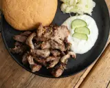 Saftiges Gyros vom Grill mit Tzatziki, Krautsalat und einem Brötchen auf schwarzer Platte.