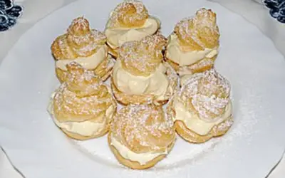 Windbeutel nach Omas Rezept, mit viel Sahne gefüllt und mit Puderzucker bestäubt, auf einem weißen Teller arrangiert.