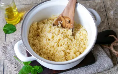 Frisch zubereiteter Couscous als Beilage in einem Topf, daneben ein Glas Öl und Minzblätter.