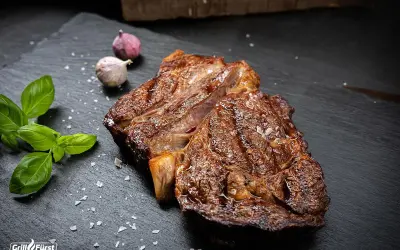 Perfekt gegrilltes Rib Eye Steak mit grobem Salz, Basilikum und Knoblauch auf schwarzem Stein.