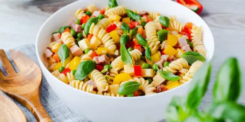 Bester Pasta Salat ohne Mayonnaise: Spiralnudeln mit Schinken, Erbsen, Paprika und Basilikum in einer weißen Schüssel.