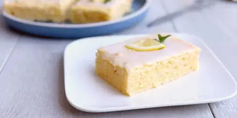 Ein Stück von Omas Zitronenkuchen vom Blech, mit Zuckerguss und Zitronenscheibe garniert.