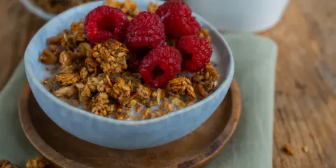 Schüssel mit selbstgemachtem Granola, Milch und frischen Himbeeren. Ein gesunder Start in den Tag!