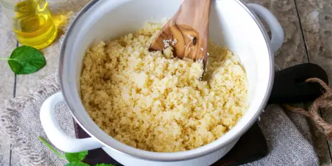 Frisch zubereiteter Couscous als Beilage in einem Topf, daneben ein Glas Öl und Minzblätter.