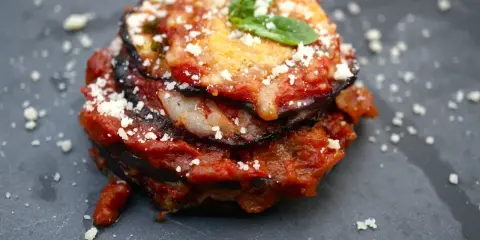 Melanzane alla Parmigiana: geschichtete Aubergine mit Tomatensauce, Käse und Basilikum, bestreut mit Parmesan.