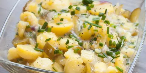 Kartoffelsalat ohne Mayo, mit Gurken, Zwiebeln und Schnittlauch in einer Glasschüssel.