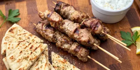 Gegrillte Souvlaki-Spieße mit Schweinefleisch, dazu Pitabrot, Tzatziki und Zitrone.