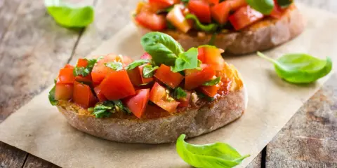 Zwei Bruschetta mit Tomaten und Basilikum, ein authentisches italienisches Rezept, auf rustikalem Holz.