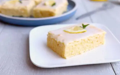 Ein Stück von Omas Zitronenkuchen vom Blech, mit Zuckerguss und Zitronenscheibe garniert.