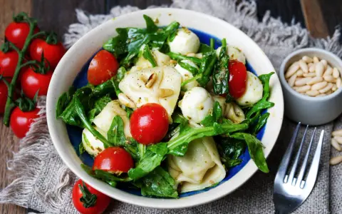 Ein köstlicher tortellini salat mit pesto, garniert mit Kirschtomaten, Mozzarella-Kugeln und Pinienkernen.