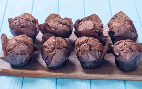 Acht schokoladige Muffins im braunen Papier auf einem Holzbrett. Perfekt für ein schokomuffins rezept.