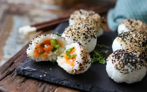 Leckere Onigiri selber machen: Reisbällchen mit Lachsfüllung, umhüllt von schwarzem und weißem Sesam.