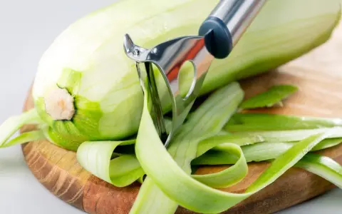 Zucchini wird geschält, aber man kann Zucchini mit Schale essen. Die grünen Streifen der Schale liegen auf dem Holzbrett.