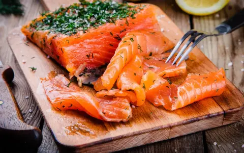 Frisch gebeizter Lachs mit Dill und Salz auf einem Holzbrett. Eine Gabel nimmt ein Stück Lachs auf.