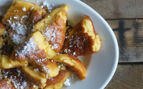 Ein Teller mit goldbraunem Kaiserschmarrn, bestäubt mit Puderzucker. Dieses Kaiserschmarrn Rezept ist ein Genuss!